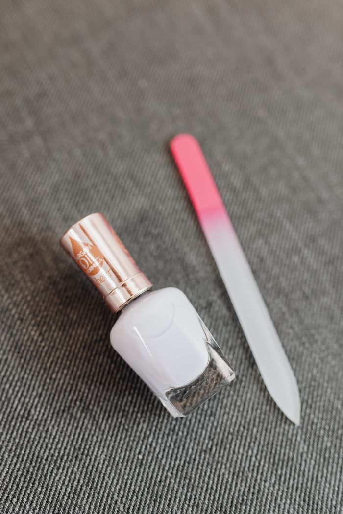 Still life of white nail polish and glass nail file on gray fabric creating a minimalist aesthetic.