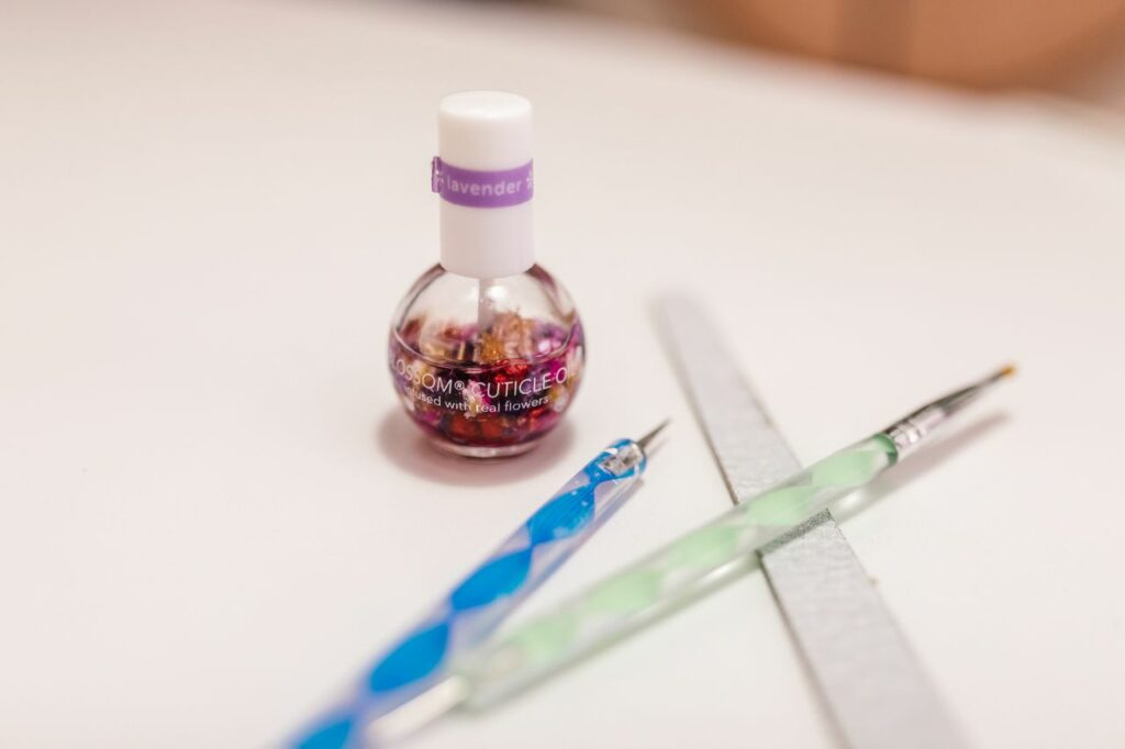 Artistic display of cuticle oil with nail art tools on a white surface.