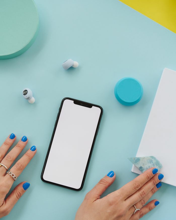 Flat lay of smartphone with blank screen and wireless earbuds on a blue background.