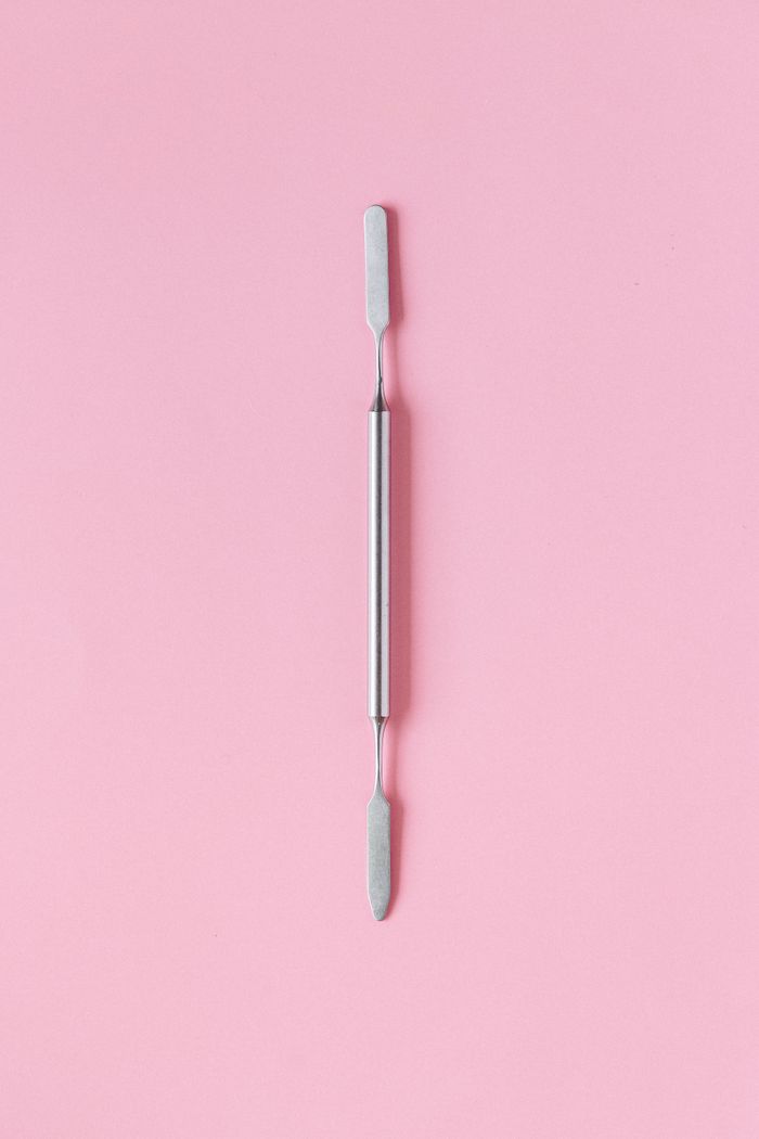 Minimalist image of a stainless steel tool on a pink background, top view.